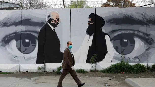 An Afghan man wearing a protective face mask walks past a wall painted with photo of Zalmay Khalilzad, US envoy for peace in Afghanistan, and Mullah Abdul Ghani Baradar, the leader of the Taliban delegation, in Kabul, Afghanistan. [IC: REUTERS]