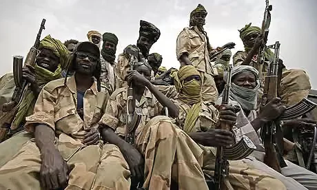A group of armed fighters wearing military uniforms and headscarves pose together holding rifles, likely in a conflict zone.