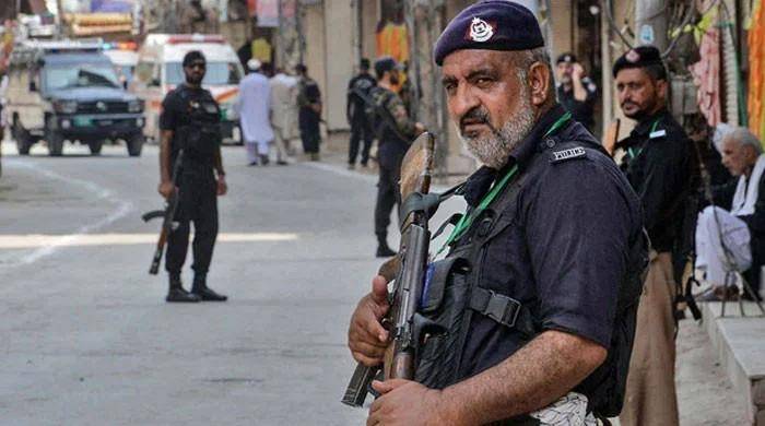 Pakistani police officers standing guard on a street, with one officer holding a rifle in the foreground while others secure the area in the background. [Courtesy: 24 NEWS].