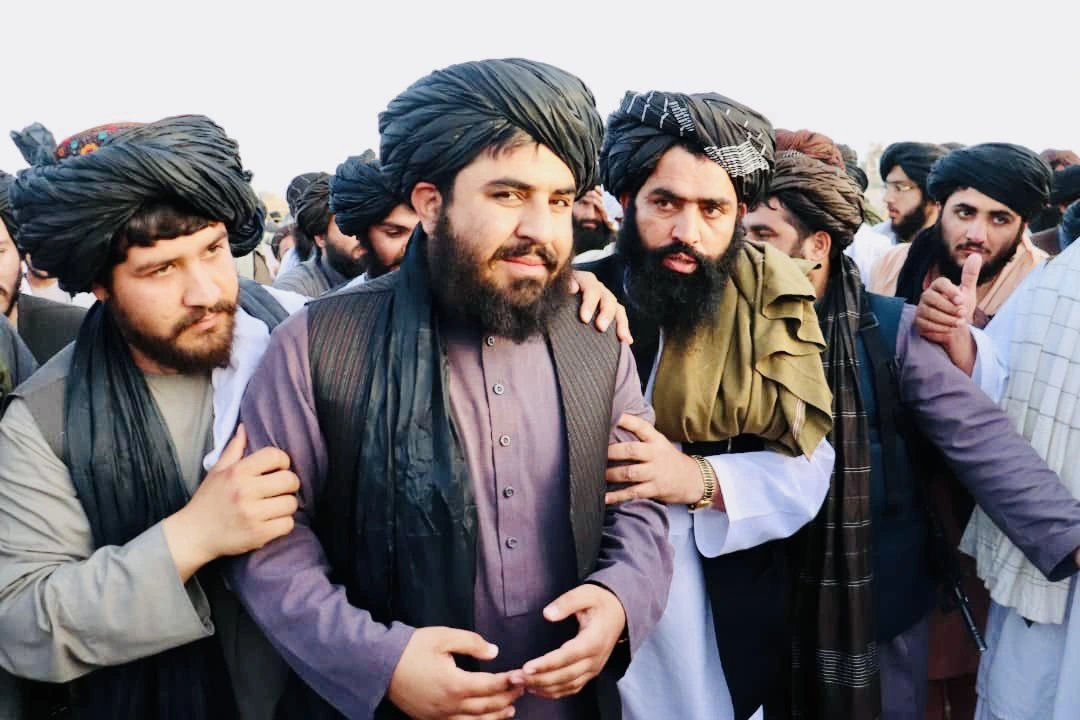 A group of Afghan men wearing traditional clothing and turbans stand closely together
