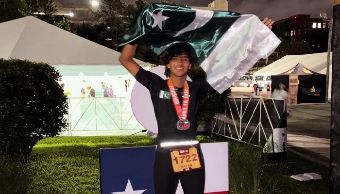 Ryan Habib crossing Ironman finish line in Texas holding Pakistani flag after completing triathlon